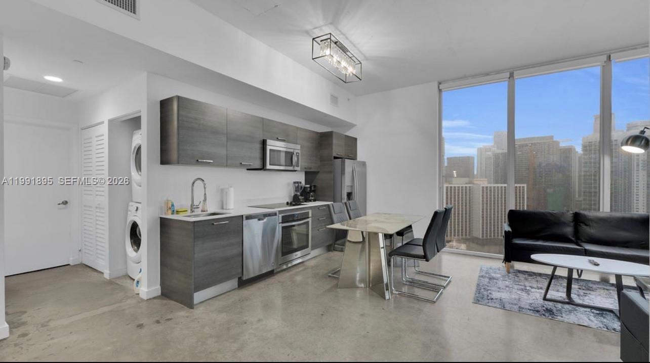 A modern kitchen and living area feature gray cabinetry, stainless steel appliances, and floor-to-ceiling windows — 151 SE 1st St # 2411, Miami FL 33131, MIAMI, FL