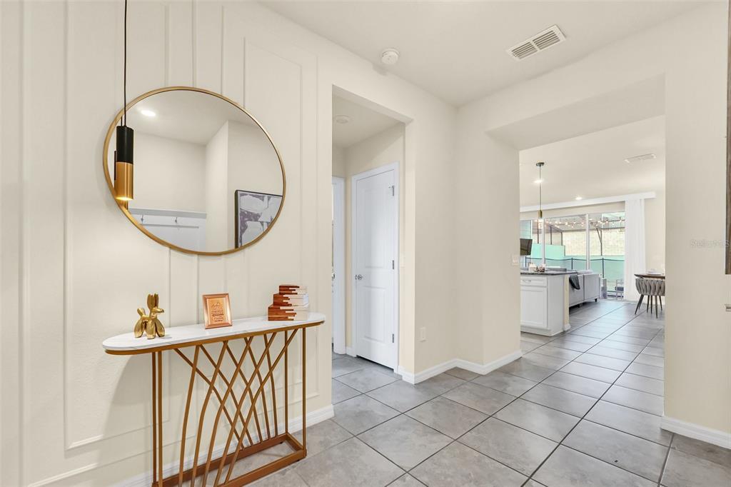 A foyer features a gold console table, a round mirror, and tile flooring leading inside — 830 PARADISE DRIVE, DAVENPORT, FL