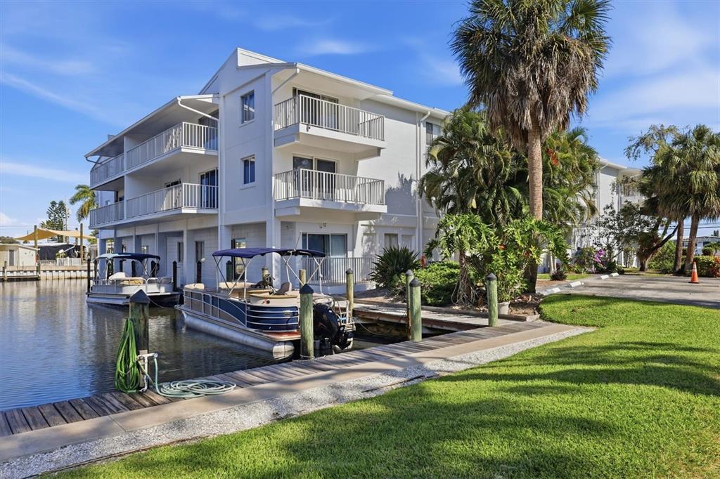 A multi-story white apartment building sits beside a canal with two docked pontoon boats — 1714 69TH AVENUE W UNIT A303, BRADENTON, FL