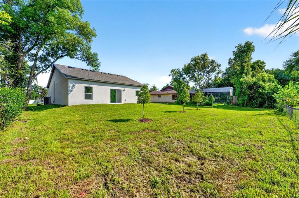 A grassy backyard features a light-colored house with a sliding glass door and nearby trees — 1669 MONTAGUE STREET, DELTONA, FL