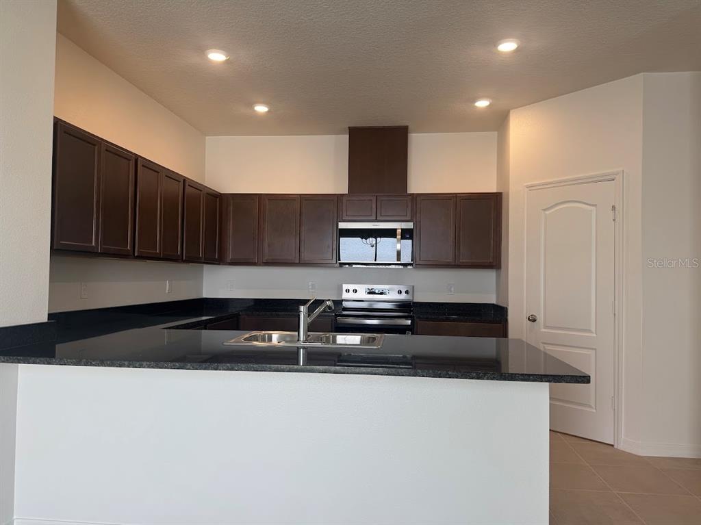 A kitchen features dark wood cabinets, black granite countertops, and stainless steel appliances — 2723 PLOVER STREET, ST CLOUD, FL