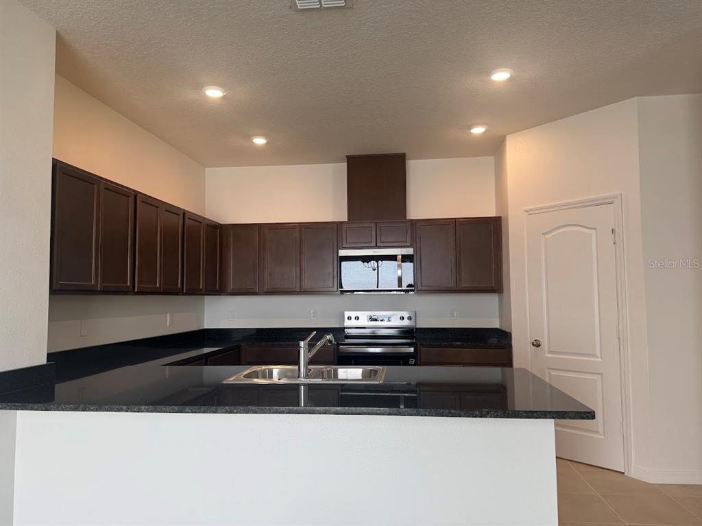 A kitchen features dark wood cabinets, black granite countertops, and stainless steel appliances — 2723 PLOVER STREET, ST CLOUD, FL