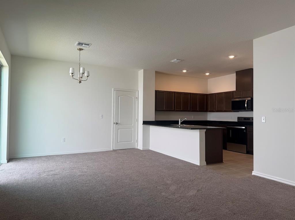 An open-concept living area features carpeted flooring, a dining chandelier, and a kitchen with dark cabinetry — 2723 PLOVER STREET, ST CLOUD, FL