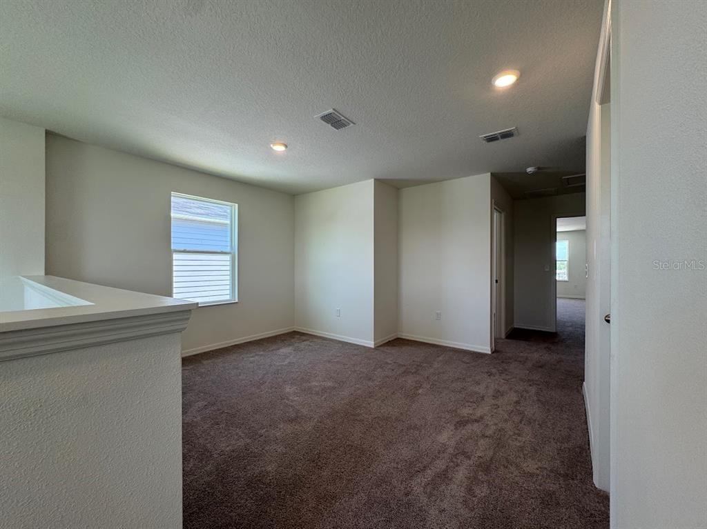 An empty carpeted loft area features a window, recessed lighting, and a hallway entrance — 2723 PLOVER STREET, ST CLOUD, FL