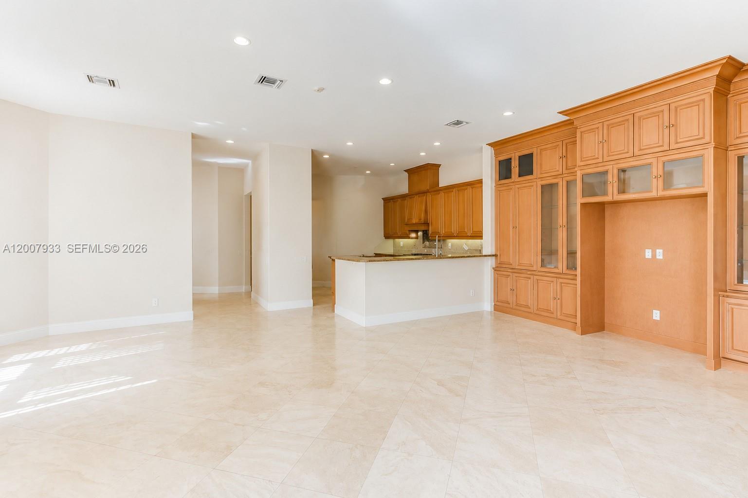 A spacious room features light tile flooring, a kitchen with wooden cabinets, and built-in shelving — 19471 NE 14th Ct, Miami FL 33179, MIAMI, FL