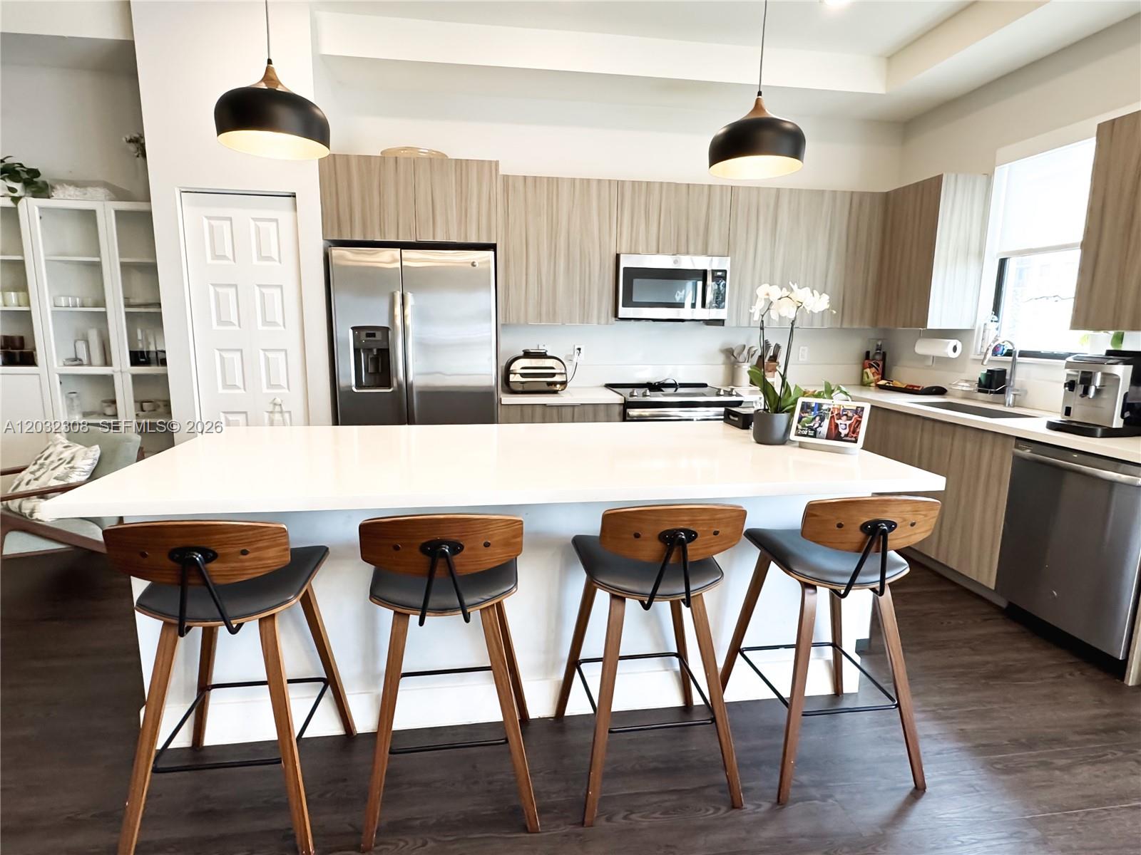 A modern kitchen features a white island with four wooden bar stools and stainless appliances — 10455 NW 82nd St # 32, Doral FL 33178, DORAL, FL