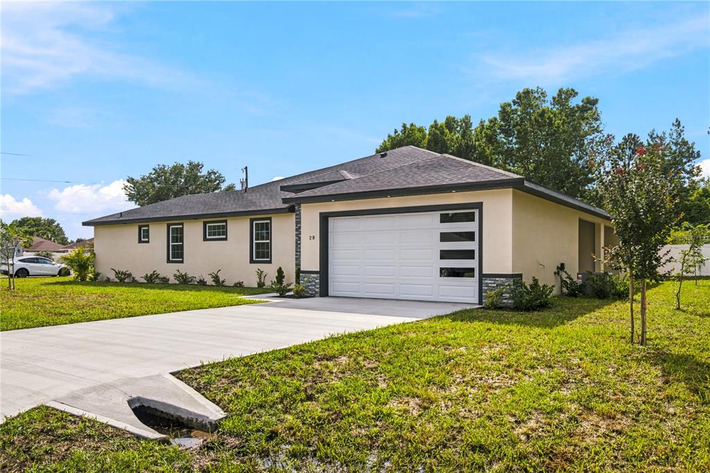 A single-story house with a white garage door, tan stucco walls, and a dark roof — 2 BUTTONBUSH LANE, PALM COAST, FL