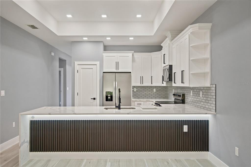 A modern kitchen features white cabinets, a marble-topped island, and a dark slatted front panel — 2 BUTTONBUSH LANE, PALM COAST, FL