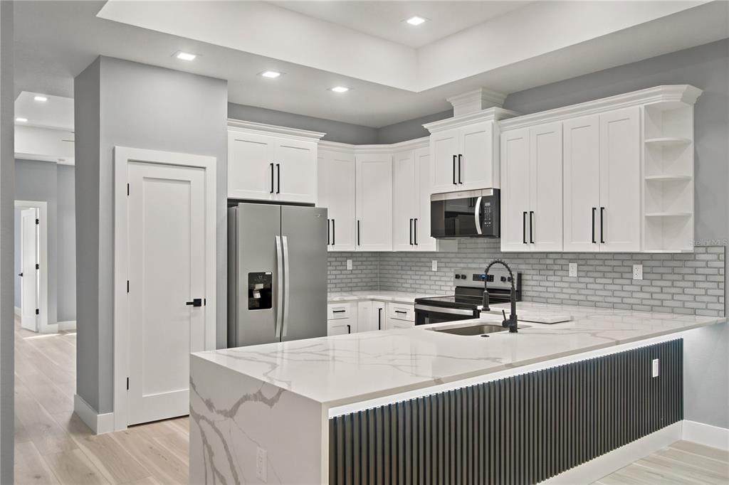 A modern kitchen features white cabinets, a marble-topped island with slatted detailing, and gray backsplash — 2 BUTTONBUSH LANE, PALM COAST, FL
