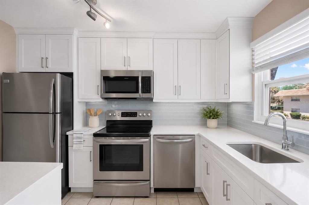 A kitchen with white cabinets, black appliances, tile countertops, and a window above the sink — 2727 75TH STREET W UNIT 8A13, BRADENTON, FL