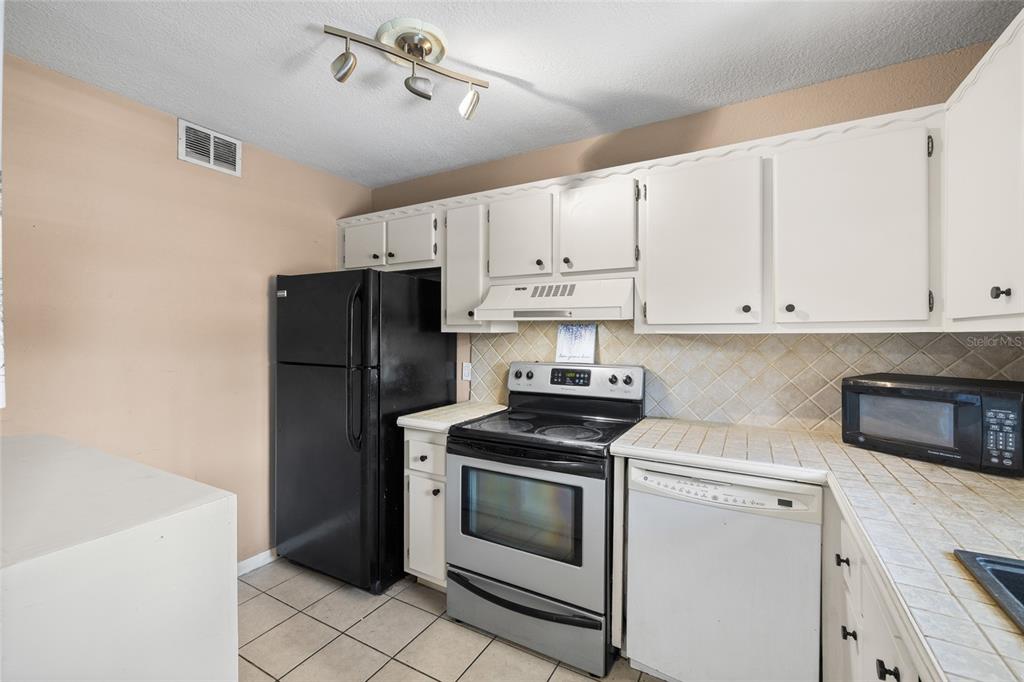 A kitchen features white cabinets, stainless steel appliances, a light blue backsplash, and white countertops — 2727 75TH STREET W UNIT 8A13, BRADENTON, FL