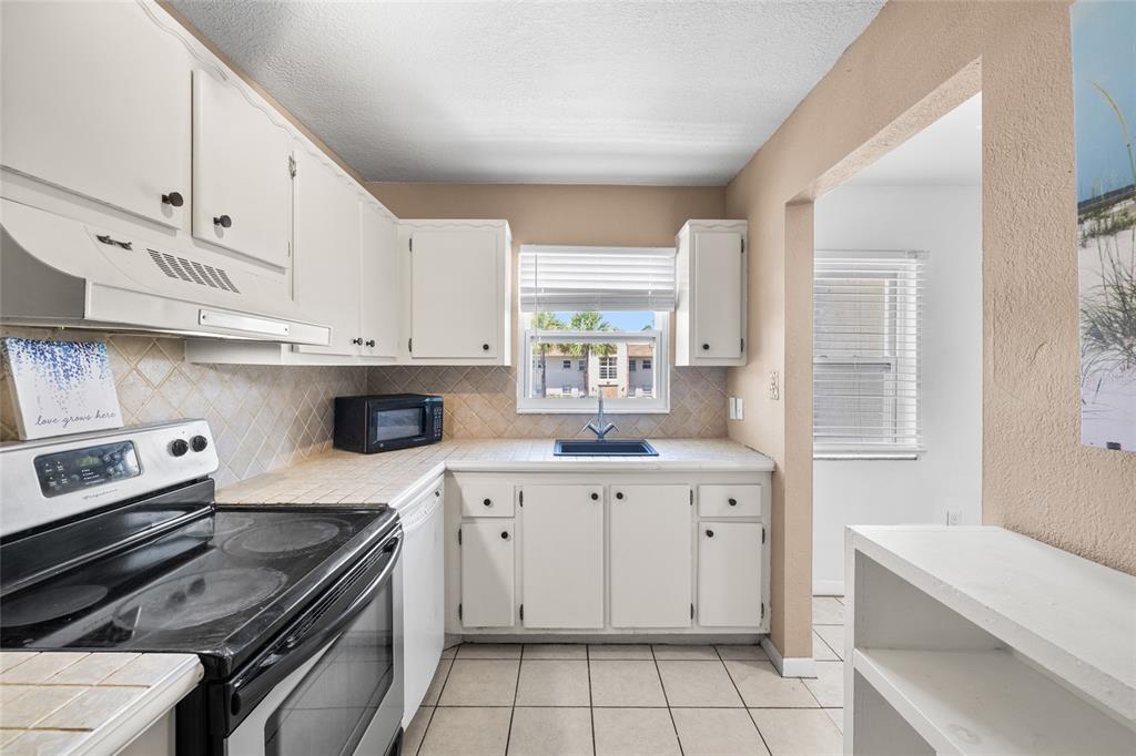 A kitchen features white cabinets, a black refrigerator, a stainless steel stove, and tiled countertops — 2727 75TH STREET W UNIT 8A13, BRADENTON, FL