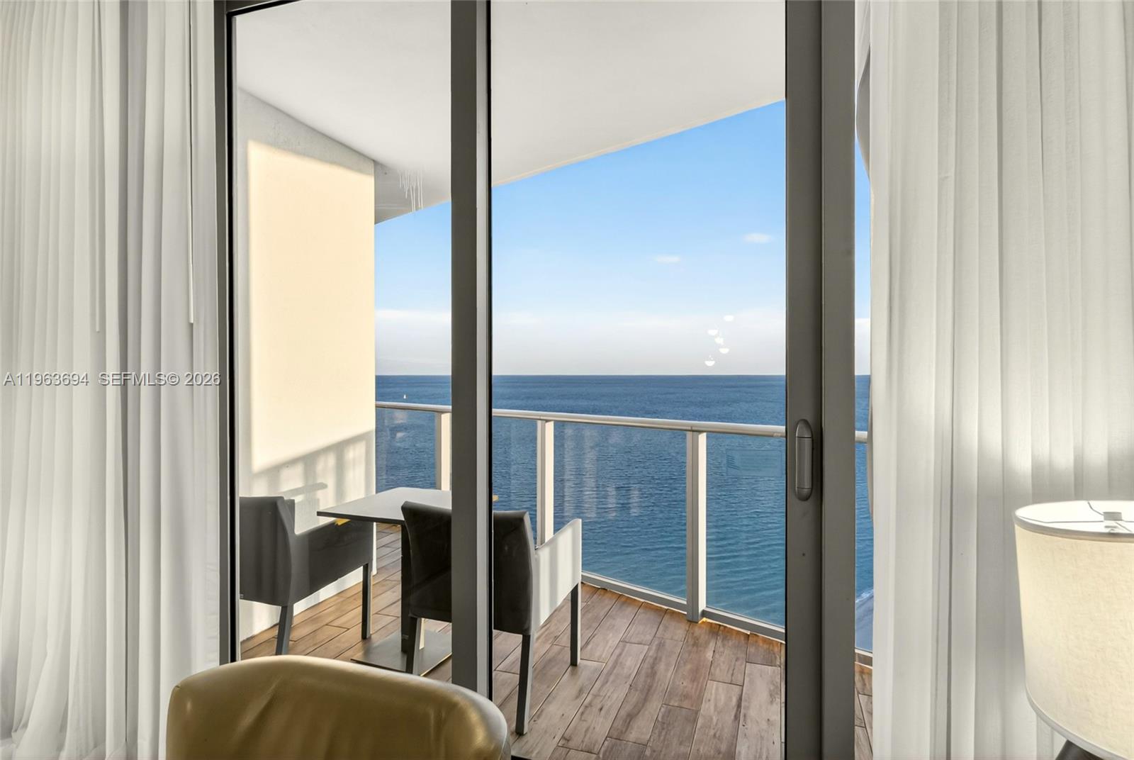 A balcony with a table and chairs overlooks the ocean through sliding glass doors — 4111 S Ocean Dr # 3703, Hollywood FL 33019, HOLLYWOOD, FL