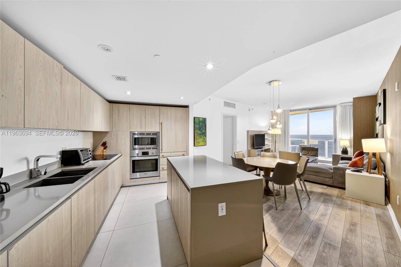 A modern kitchen with light wood cabinetry and a central island overlooks a dining area — 4111 S Ocean Dr # 3703, Hollywood FL 33019, HOLLYWOOD, FL