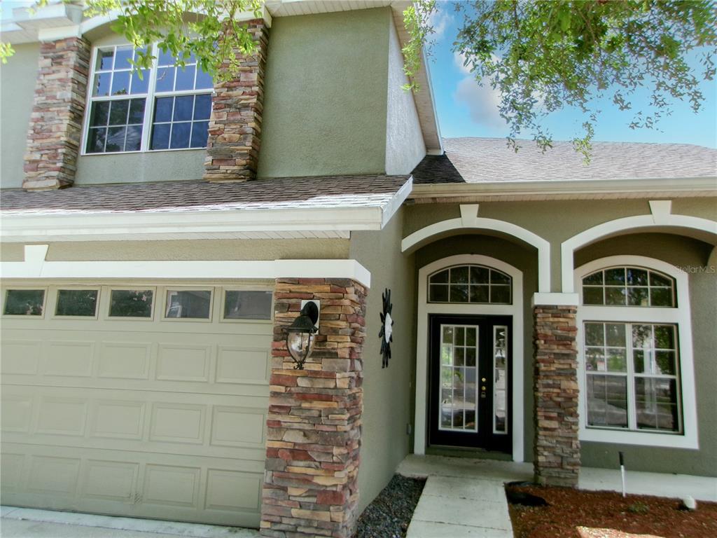 A two-story house exterior features a garage, stone accents, and a front entryway with windows — 11314 OYSTER BAY CIRCLE, NEW PORT RICHEY, FL