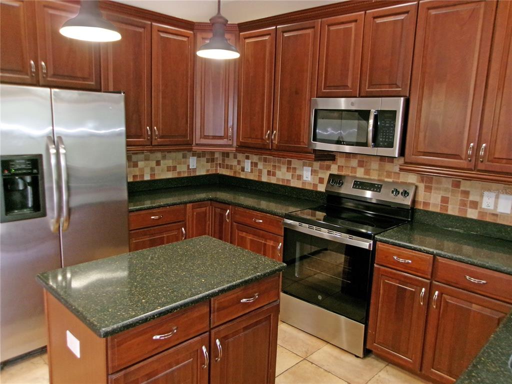 A kitchen features dark wood cabinets, granite countertops, stainless steel appliances, and a center island — 11314 OYSTER BAY CIRCLE, NEW PORT RICHEY, FL