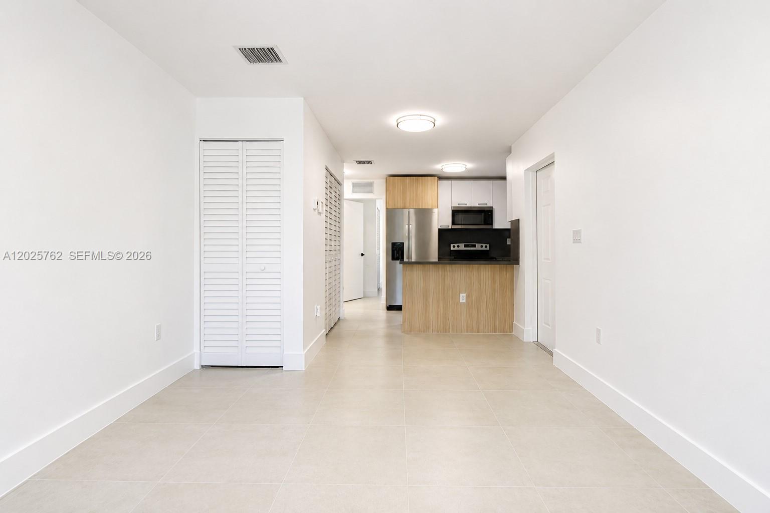 A kitchen with light wood cabinetry and stainless steel appliances opens to a tiled room — 1834 NW 63rd St # 1834, Miami FL 33147, MIAMI, FL