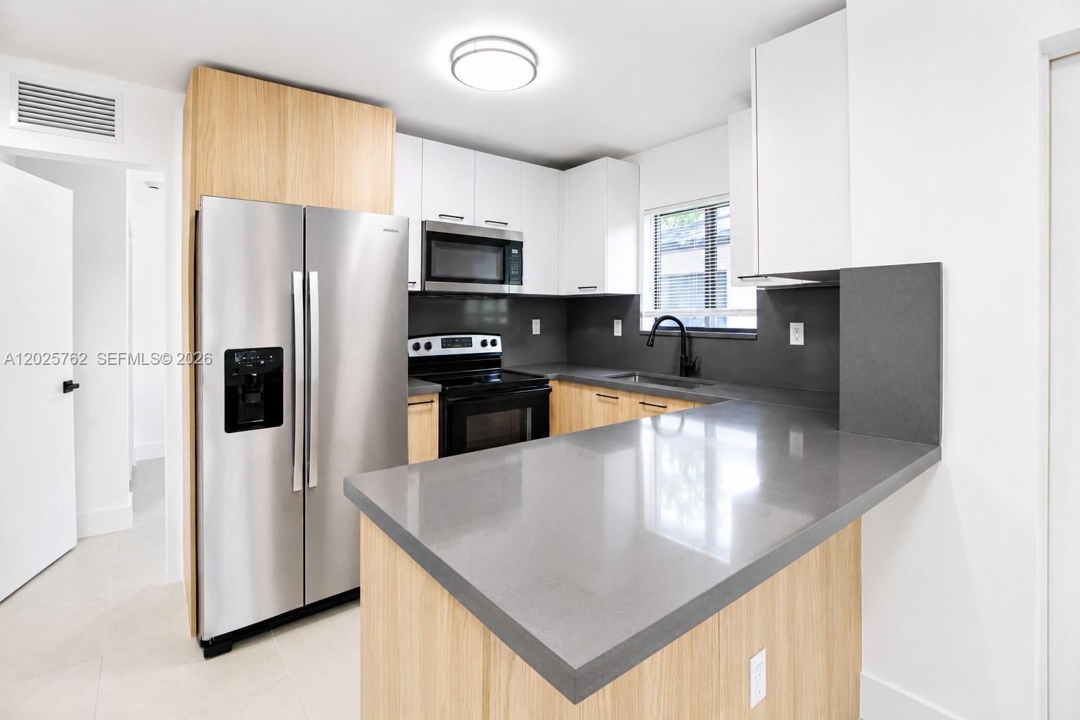 A modern kitchen features light wood cabinets, white upper cabinets, and gray quartz countertops — 1834 NW 63rd St # 1834, Miami FL 33147, MIAMI, FL