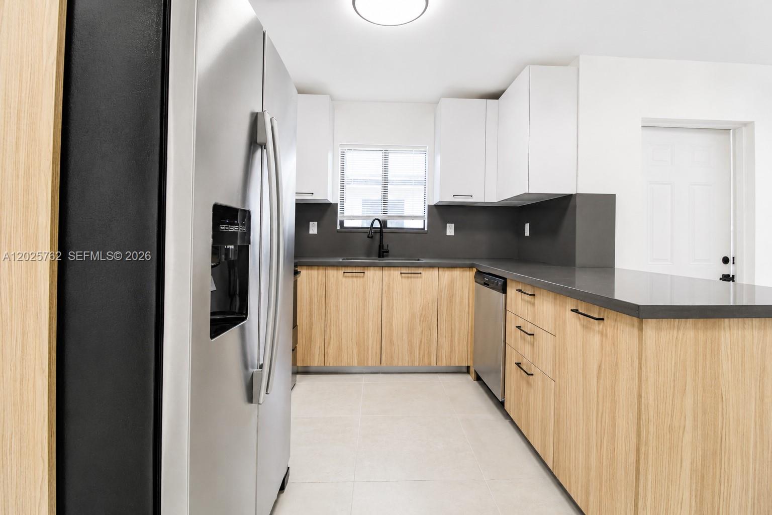 A modern kitchen features light wood cabinets, white upper cabinets, and dark gray countertops — 1834 NW 63rd St # 1834, Miami FL 33147, MIAMI, FL