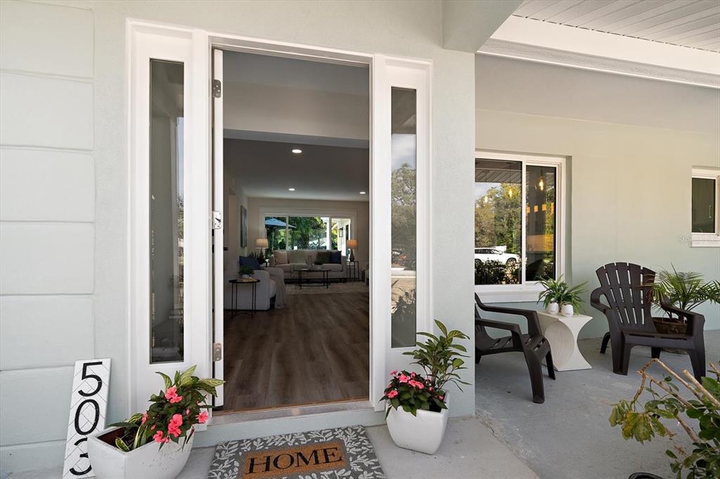The front entrance of a house features a glass-paneled door, potted plants, and outdoor seating — 503 POINSETTIA ROAD, BELLEAIR, FL
