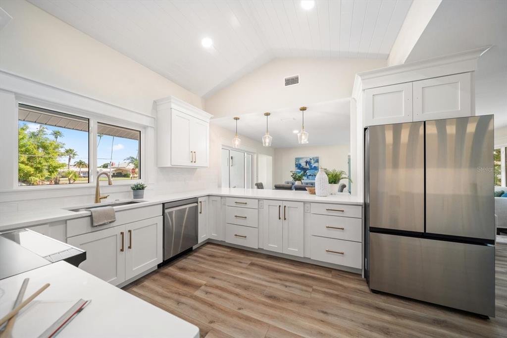A modern kitchen features white cabinetry, stainless steel appliances, and wood-look flooring under a vaulted ceiling — 503 POINSETTIA ROAD, BELLEAIR, FL