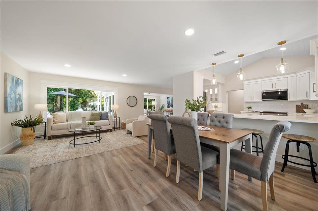 An open-concept living and dining area features light wood flooring, white cabinetry, and neutral furniture — 503 POINSETTIA ROAD, BELLEAIR, FL