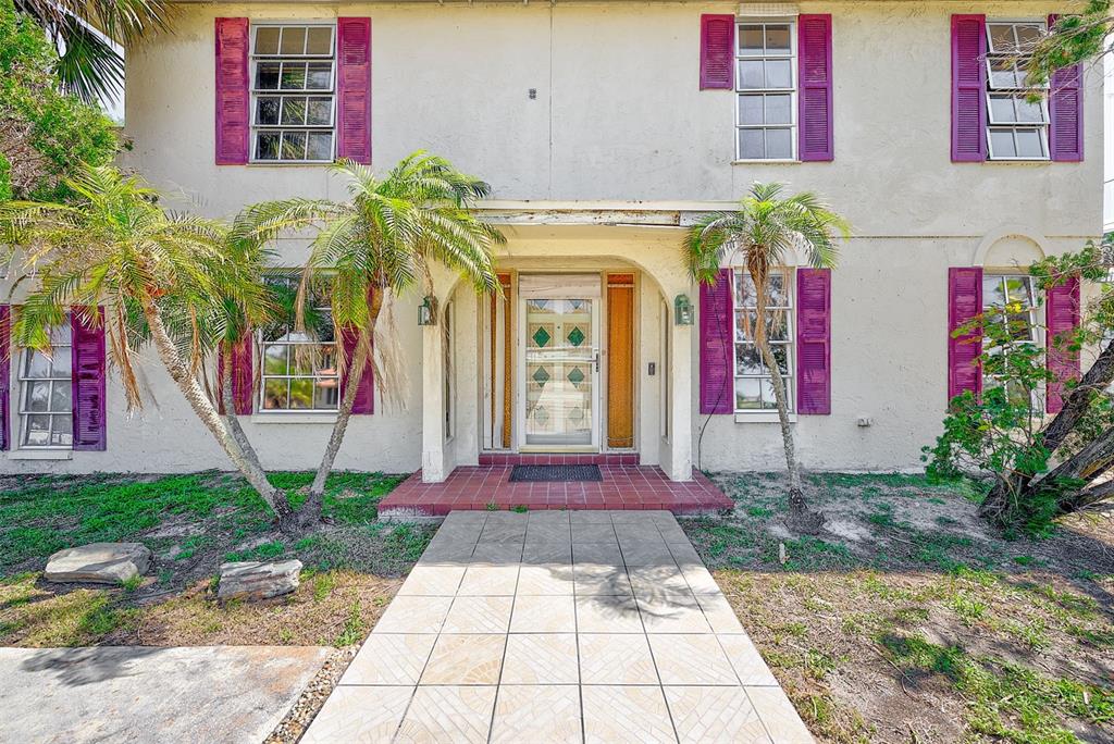 A two-story house exterior features a tiled walkway, arched entryway, and purple window shutters — 205 GULF BOULEVARD, BELLEAIR BEACH, FL