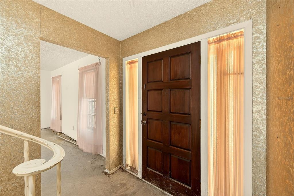 An entryway features a dark wood front door with sidelights, gold wallpaper, and a staircase — 205 GULF BOULEVARD, BELLEAIR BEACH, FL