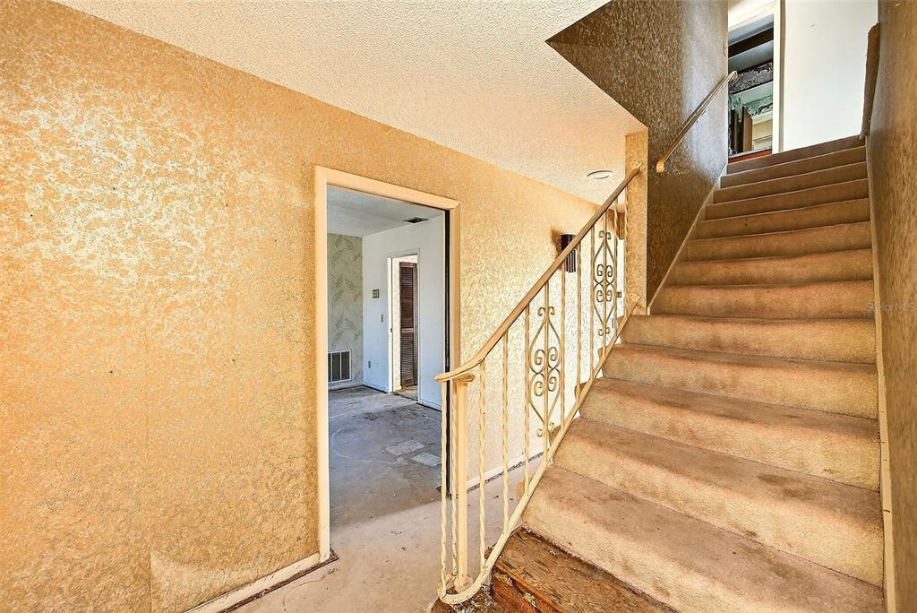 A carpeted staircase with a decorative metal railing stands next to a room with textured wallpaper — 205 GULF BOULEVARD, BELLEAIR BEACH, FL