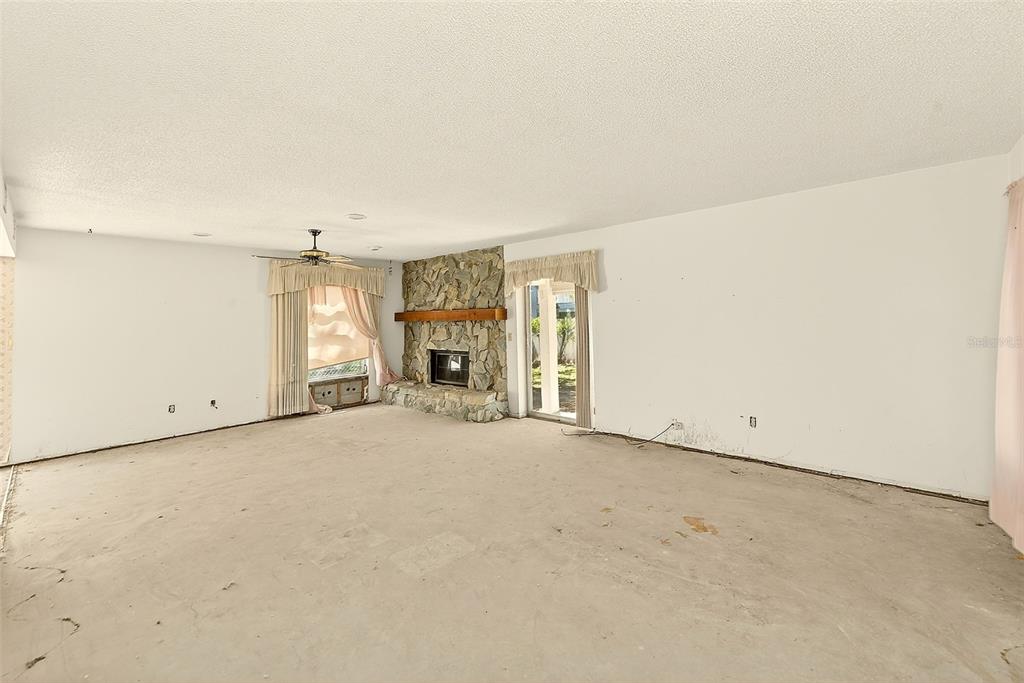 An empty living room with a stone fireplace, sliding glass doors, and bare concrete floors — 205 GULF BOULEVARD, BELLEAIR BEACH, FL