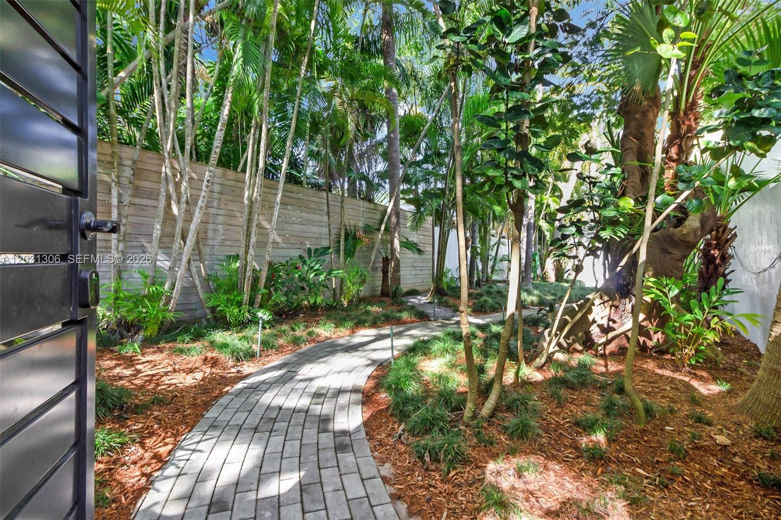 A paved walkway winds through a lush, landscaped garden enclosed by a wooden fence — 4051 Ensenada Avenue, Miami FL 33133, MIAMI, FL