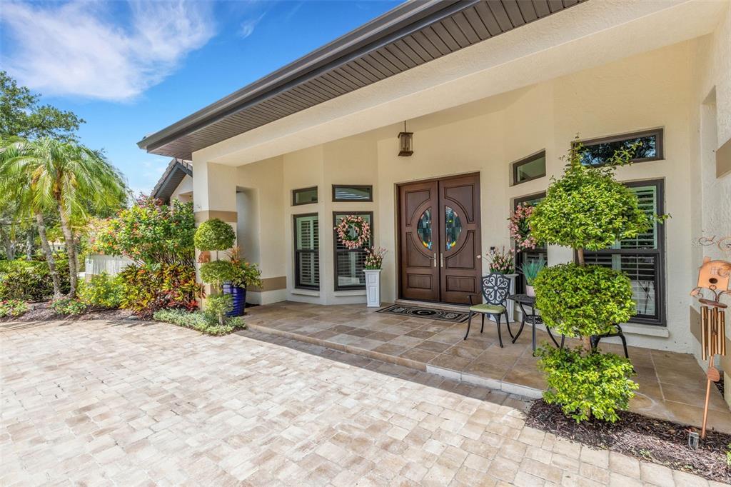 A paved driveway leads to the covered front porch and double wooden doors of a house — 7732 DONALD ROSS ROAD W, SARASOTA, FL