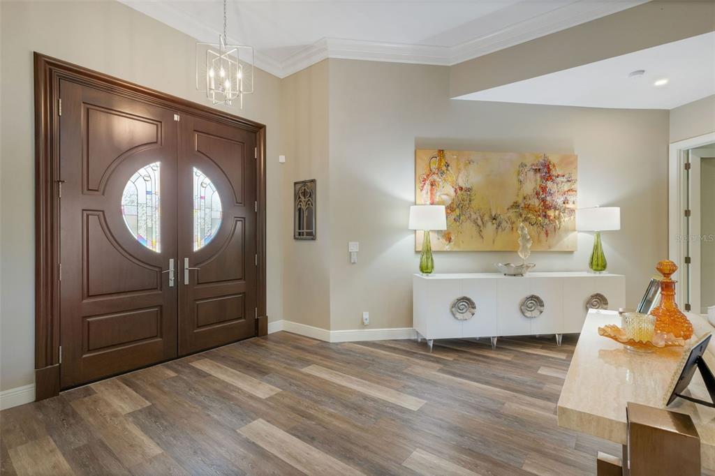 A foyer features double wood doors, wood-look flooring, a white console table, and wall art — 7732 DONALD ROSS ROAD W, SARASOTA, FL