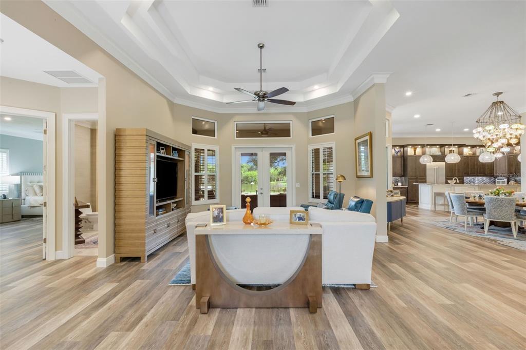 A living room with a tray ceiling, wood-look flooring, and an open view to the kitchen — 7732 DONALD ROSS ROAD W, SARASOTA, FL