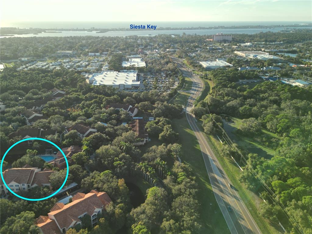 An aerial view shows a residential complex with a pool, surrounded by trees and roads — 4178 CENTRAL SARASOTA PARKWAY UNIT 323, SARASOTA, FL