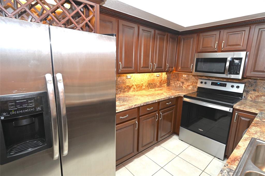 A kitchen features stainless steel appliances, dark wood cabinets, and granite countertops — 4178 CENTRAL SARASOTA PARKWAY UNIT 323, SARASOTA, FL
