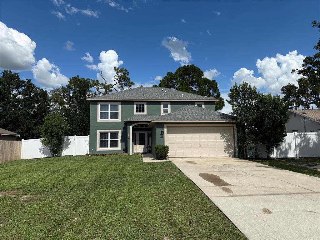 A two-story green house with a tan-trimmed front door and a small garden bed — 10056 GIFFORD STREET, SPRING HILL, FL