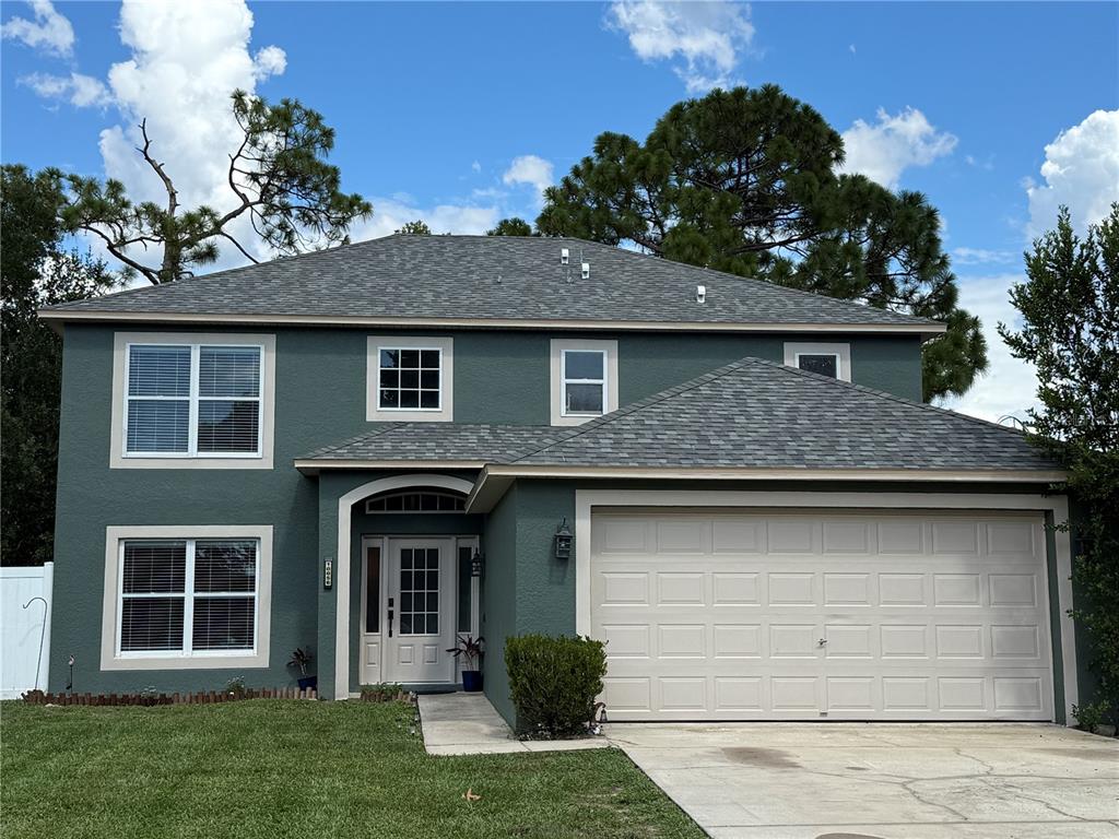 A green house exterior features a front garden bed with mulch, shrubs, and a hanging planter — 10056 GIFFORD STREET, SPRING HILL, FL