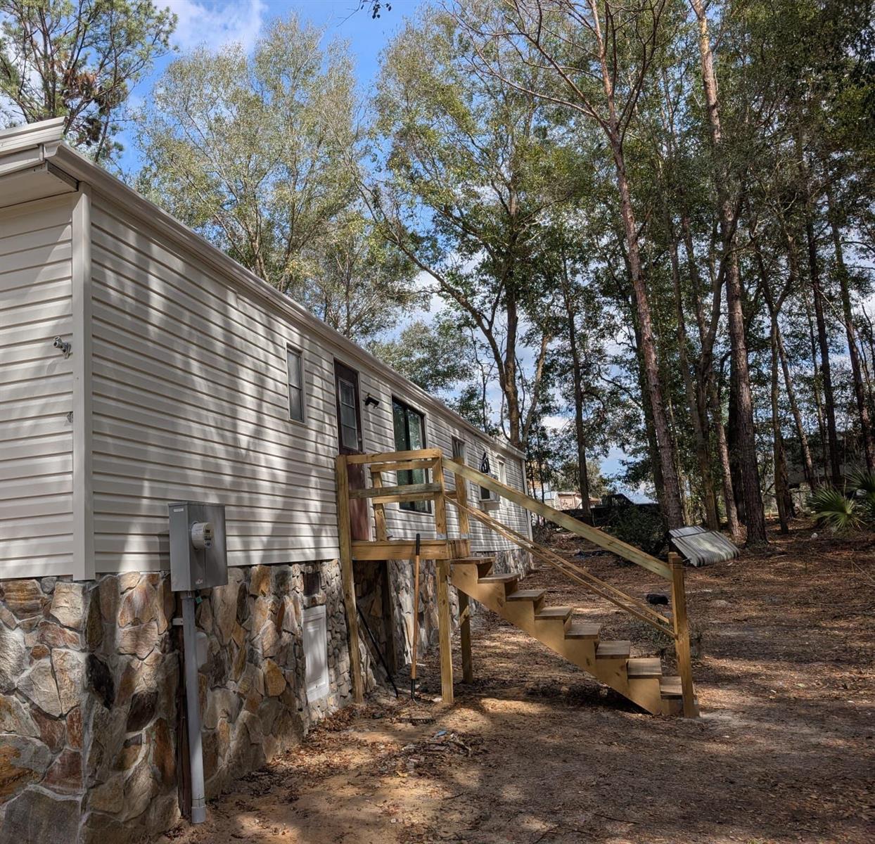 Exterior view of a manufactured home with beige siding, stone skirting, and wooden stairs — 134 John Street, FL 32640, FL