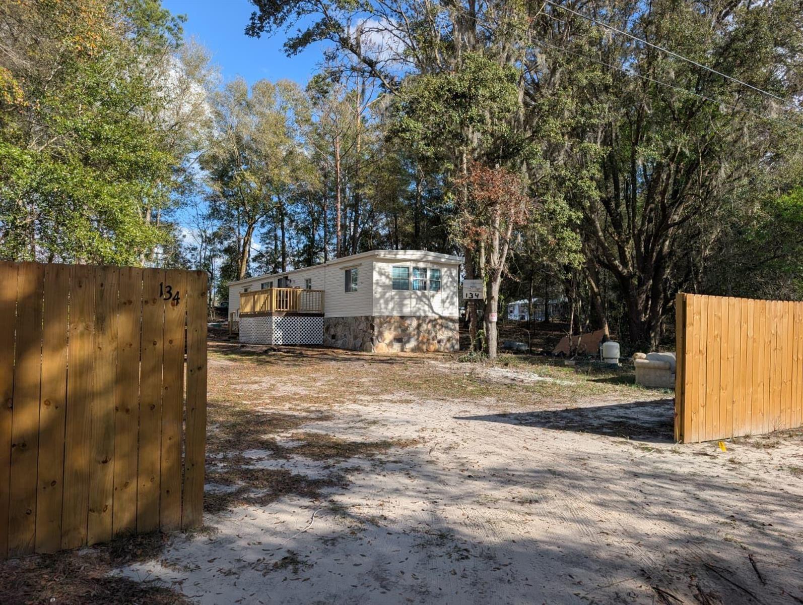 A mobile home with a wooden deck and stone skirting sits behind a wooden fence — 134 John Street, FL 32640, FL