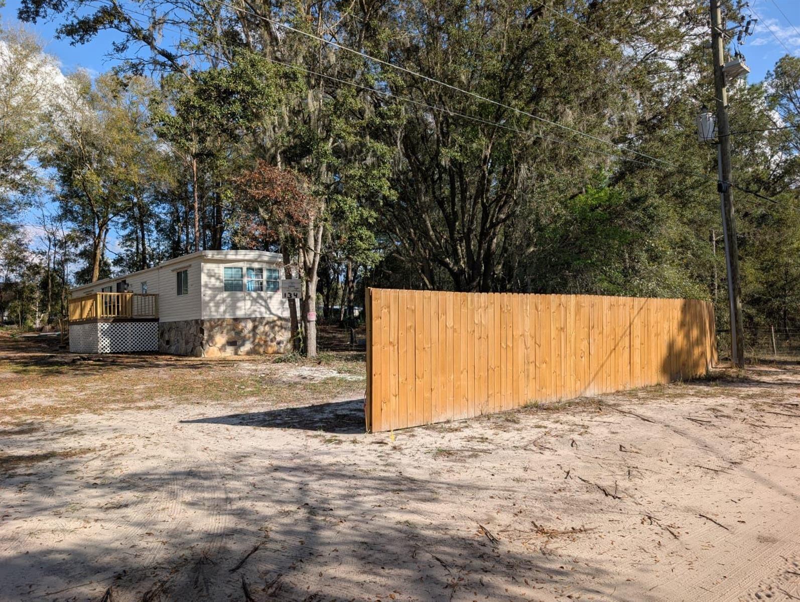 A mobile home with a wooden deck sits behind a tall wooden privacy fence — 134 John Street, FL 32640, FL