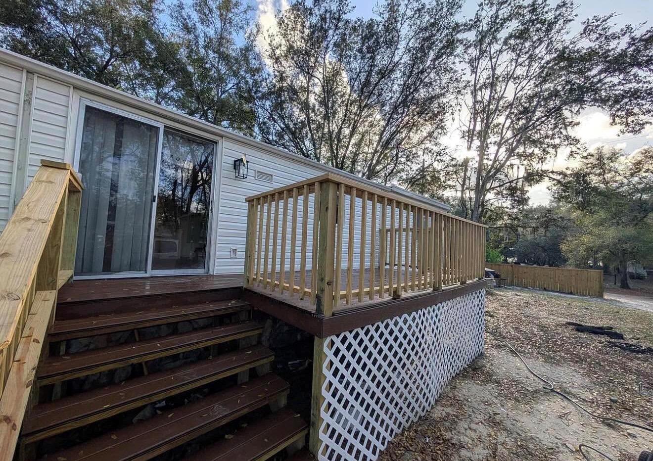 A wooden deck with railings and stairs sits outside a mobile home with white siding — 134 John Street, FL 32640, FL