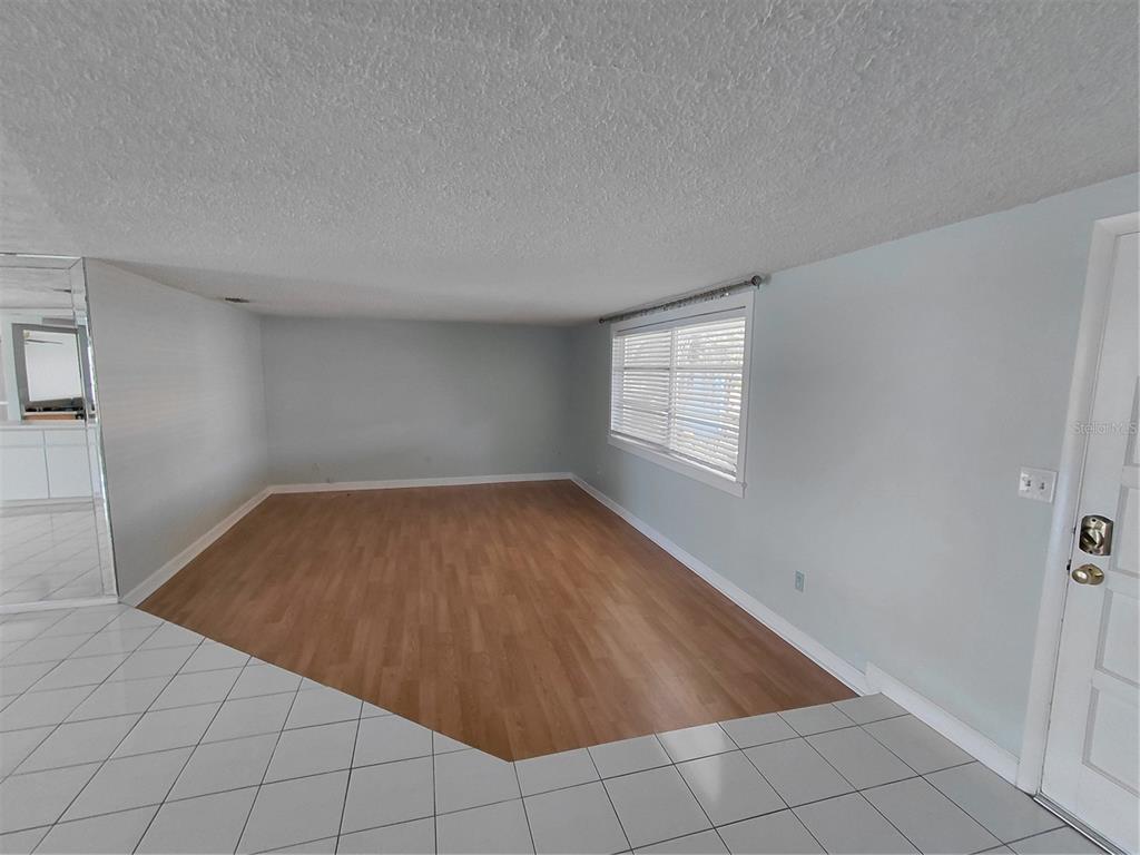 An empty living room features light wood-look flooring, white walls, and a large window — 4113 STAR ISLAND DRIVE, HOLIDAY, FL