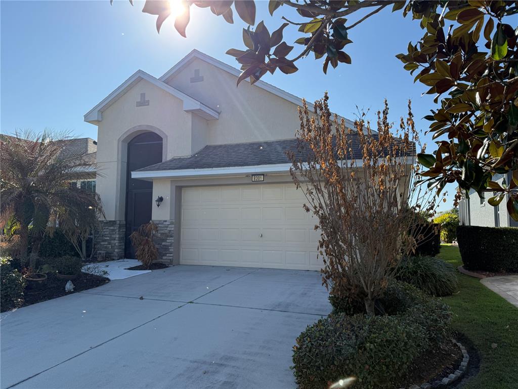 A beige single-story house with a two-car garage, stone accents, and a landscaped front yard — 8301 BRIDGEPORT BAY CIRCLE, MOUNT DORA, FL