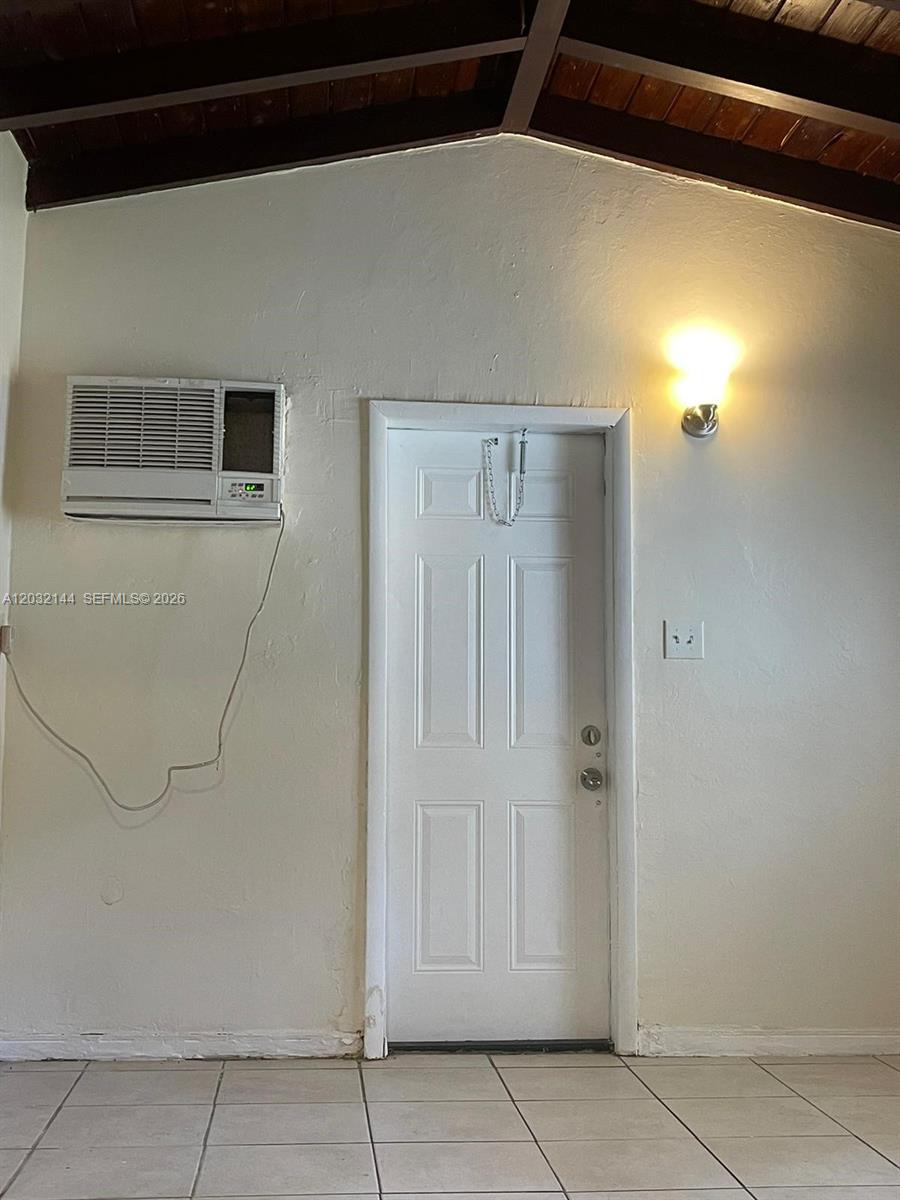 A room features a white door, a wall-mounted air conditioner, and a wooden beamed ceiling — MIAMI, FL