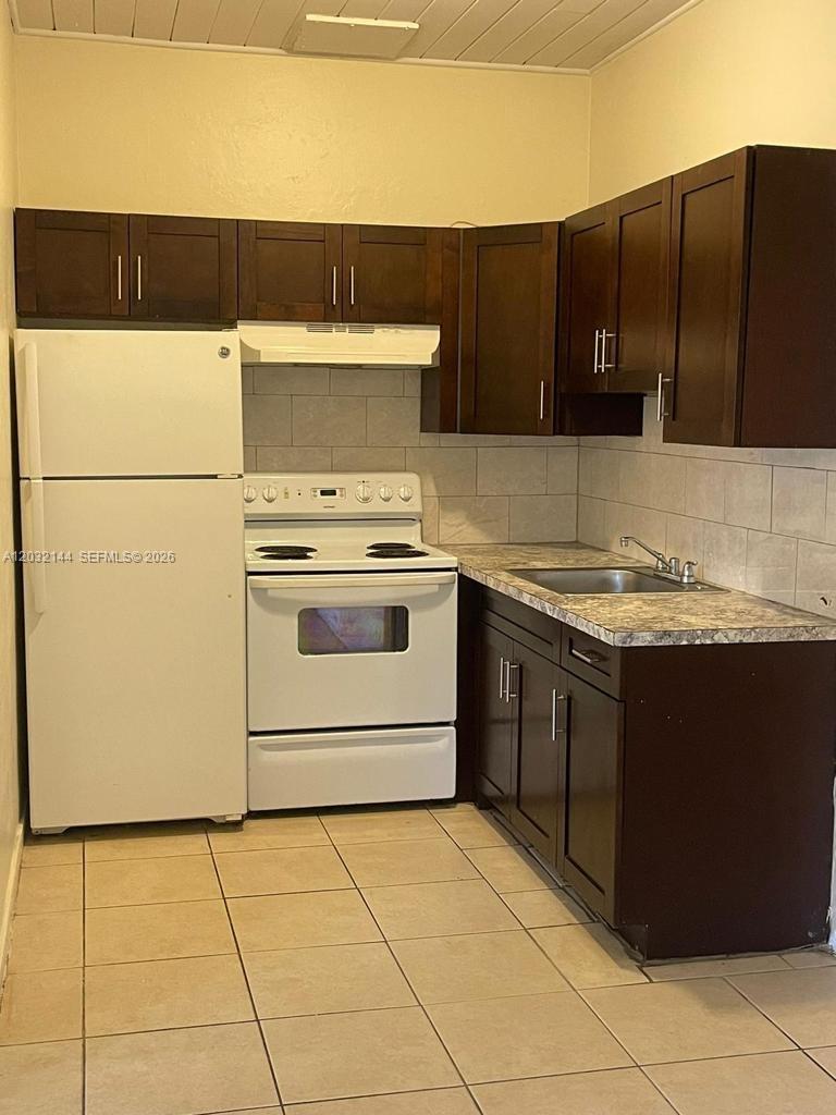 A small kitchen features dark wood cabinets, a white stove, and a white refrigerator — MIAMI, FL