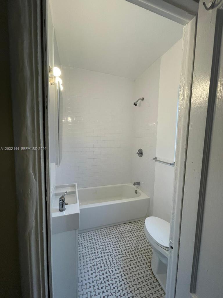 A small bathroom features a white subway-tiled tub, a pedestal sink, and patterned floor tiles — MIAMI, FL