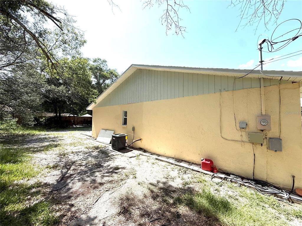 The exterior side of a yellow stucco house features a small window and HVAC unit — 6308 N 22ND STREET, TAMPA, FL