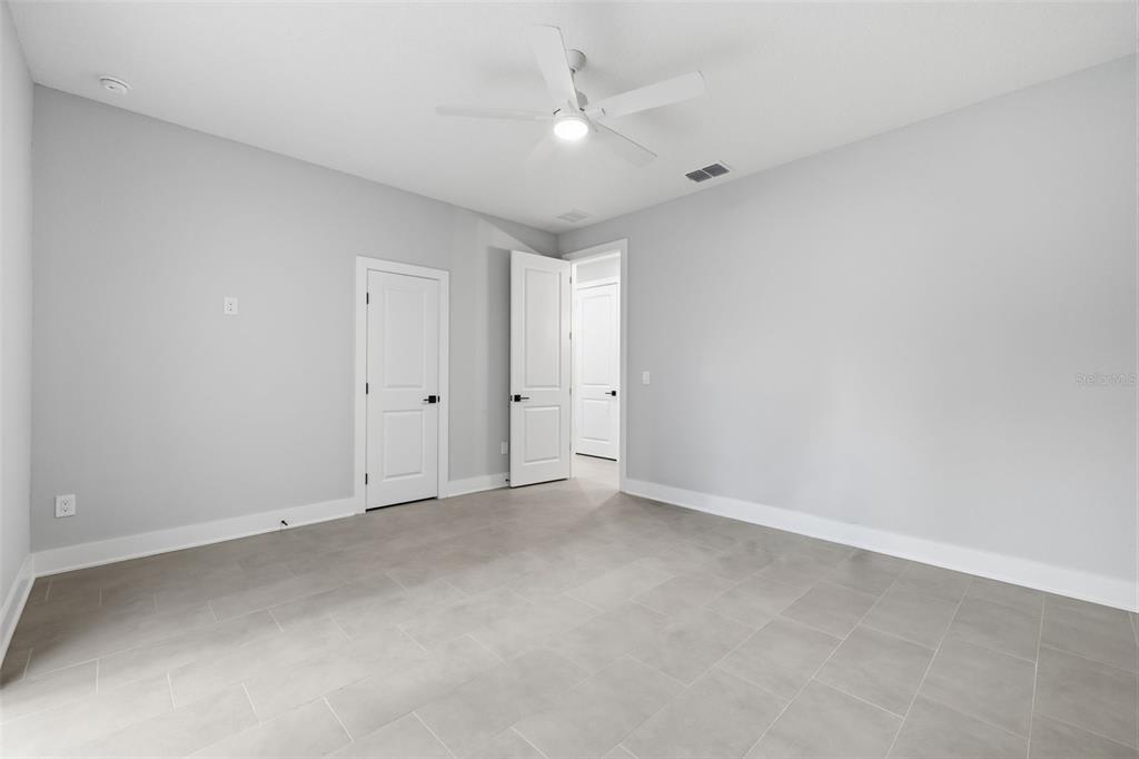 A bedroom with light gray walls, large tile flooring, a ceiling fan, and two doors — 4208 W CARMEN STREET UNIT C, TAMPA, FL