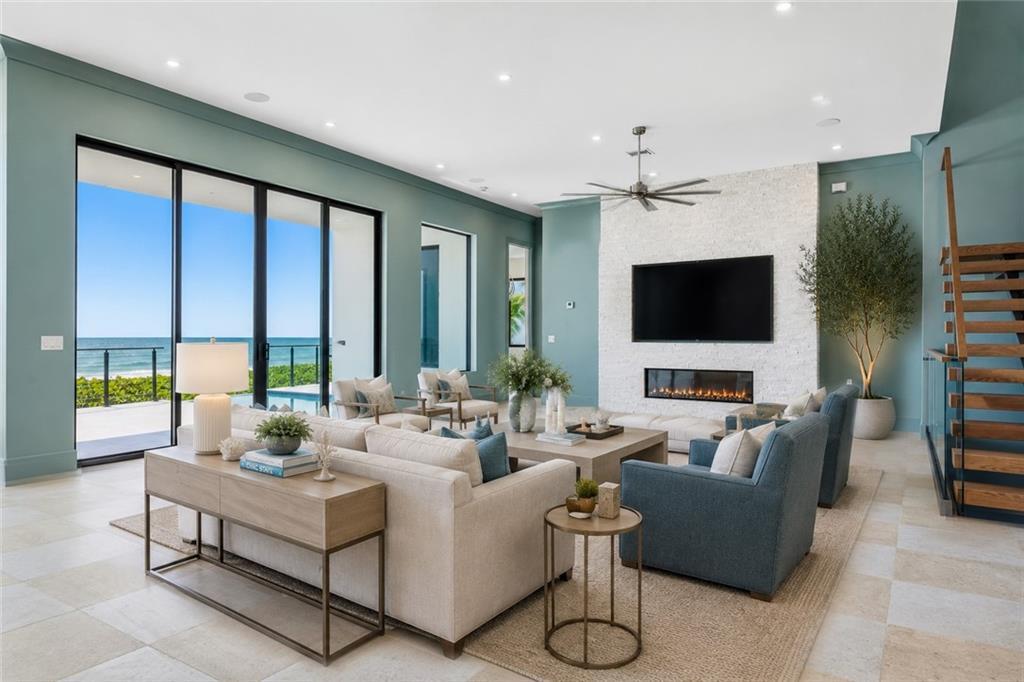 A living room features a stone fireplace, blue walls, and large sliding doors overlooking the ocean — JENSEN BEACH, FL